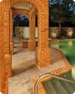 Stamped concrete pool deck in a variegated gray pattern under brick archways in Richmond VA