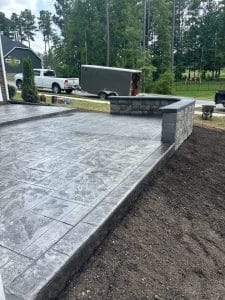 Gray stamped concrete patio with ashlar pattern and dark border next to a block retaining wall in Richmond VA