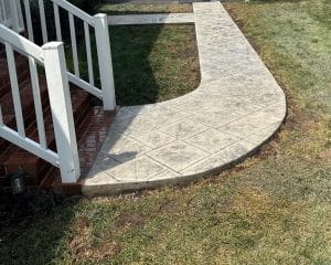 Light gray stamped concrete walkway with diamond pattern next to brick stairs and lawn in Williamsburg VA