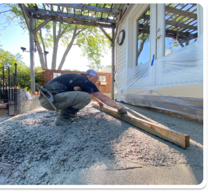 Contractor screeding wet gray concrete for a patio or walkway next to a building in Chesterfield VA