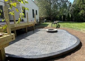 Stamped concrete patio with cobblestone pattern, dark border, and fire pit by a deck in Richmond VA