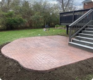 Stamped brick-patterned concrete patio next to dark wooden deck and stairs in Richmond VA