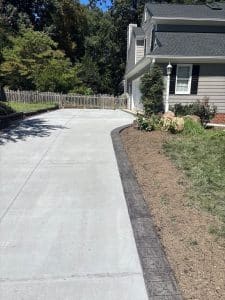 Broom-finished concrete driveway with a dark, stamped landscape border next to a house in Midlothian VA