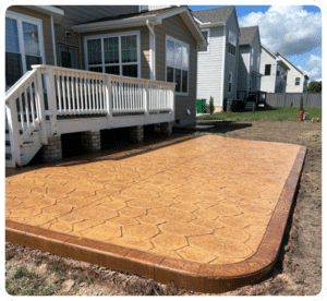 Stamped concrete patio, tan cobblestone pattern with brown border, next to a deck in Richmond VA