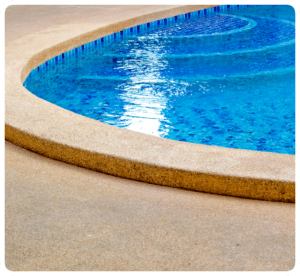 Exposed aggregate concrete pool deck with matching coping bordering a blue tiled pool in Richmond VA