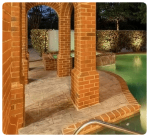 Stamped concrete path with a stone pattern next to a pool, surrounded by brick arches in Richmond VA